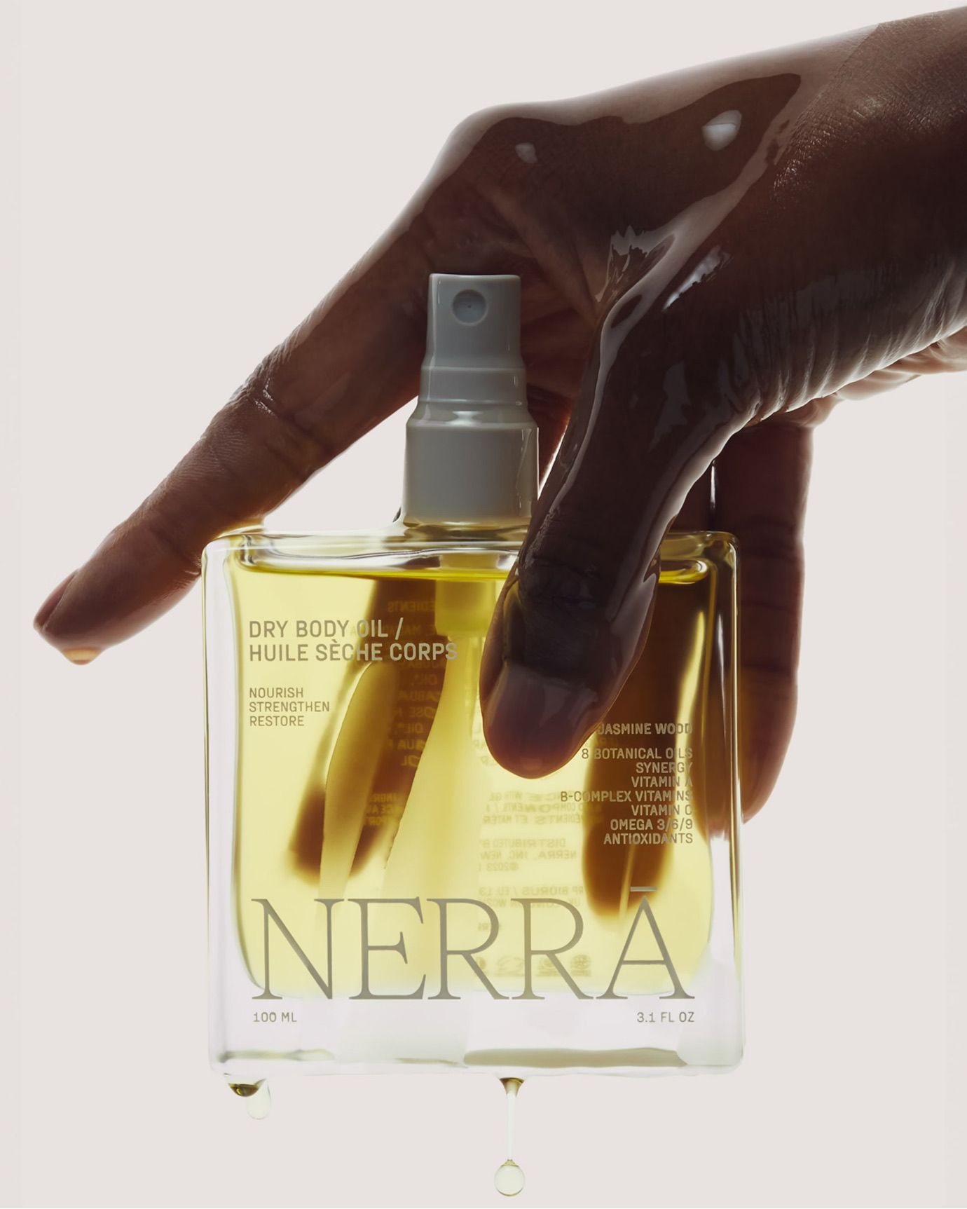 Nerra dry body oil spray bottle being held with oil dripping